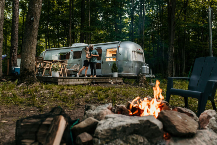 couple by airstream in front of campfire