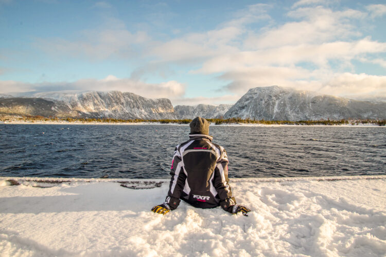 Person sitting in the snow looking out at the mountains