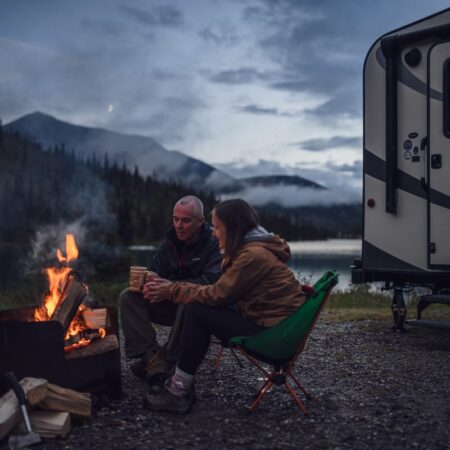 Travel trailer parked beside a lake in B.C. with campers outside enjoying a campfire
