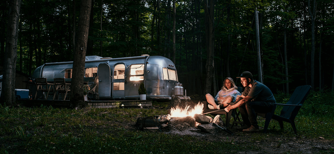 couple sitting around a campfire at dusk with an Airstream in the background