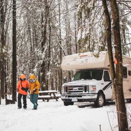 Two members of BGOW walking in the winter with an RV parked at a campsite