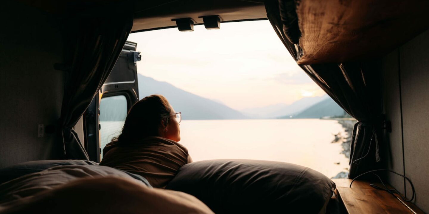 Woman lying in a camper van looking out to a lake