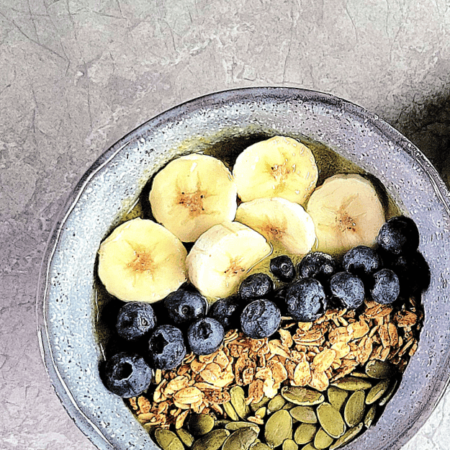 A smoothie bowl with fruit and nuts on the top and a green smoothie with pumpkin seeds on top.