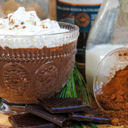 Hot chocolate in a glass mug placed on a piece of wood with chocolate and cocoa and milk.