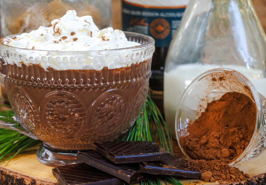 Hot chocolate in a glass mug placed on a piece of wood with chocolate and cocoa and milk.