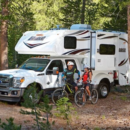 Truck camper parked at a wooded campsite with campers preparing to go on a bike ride