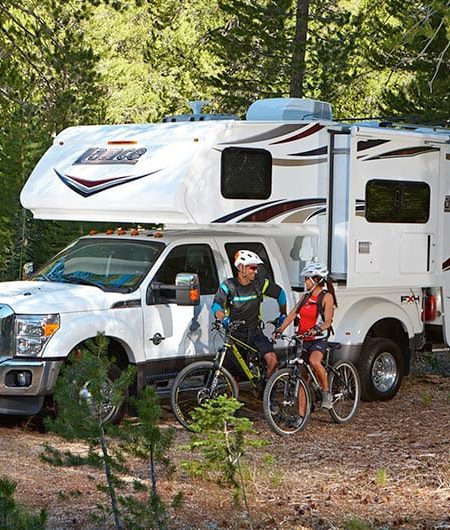 Truck camper parked at a wooded campsite with campers preparing to go on a bike ride