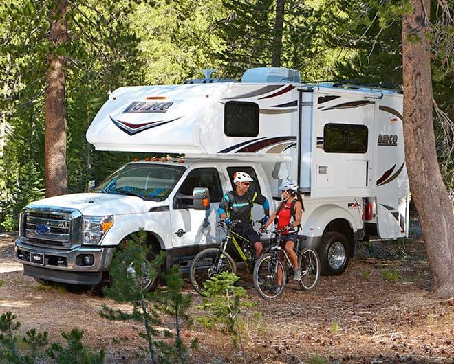Truck camper parked at a wooded campsite with campers preparing to go on a bike ride