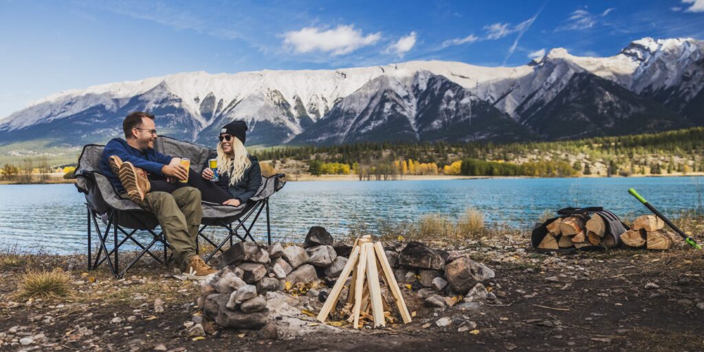 Two campers sitting outside with a canadian landscape behind them and sitting on camping chairs