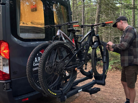 Man hooking his mountain bikes up to bike rack on the back of his RV (Class B Camper Van).