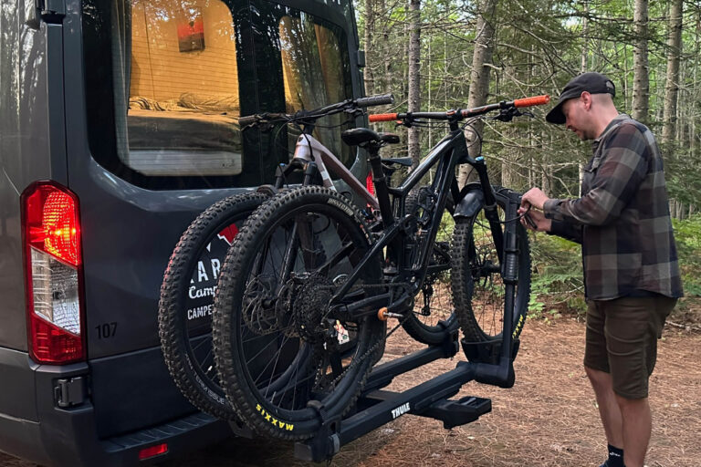Man hooking his mountain bikes up to bike rack on the back of his RV (Class B Camper Van).